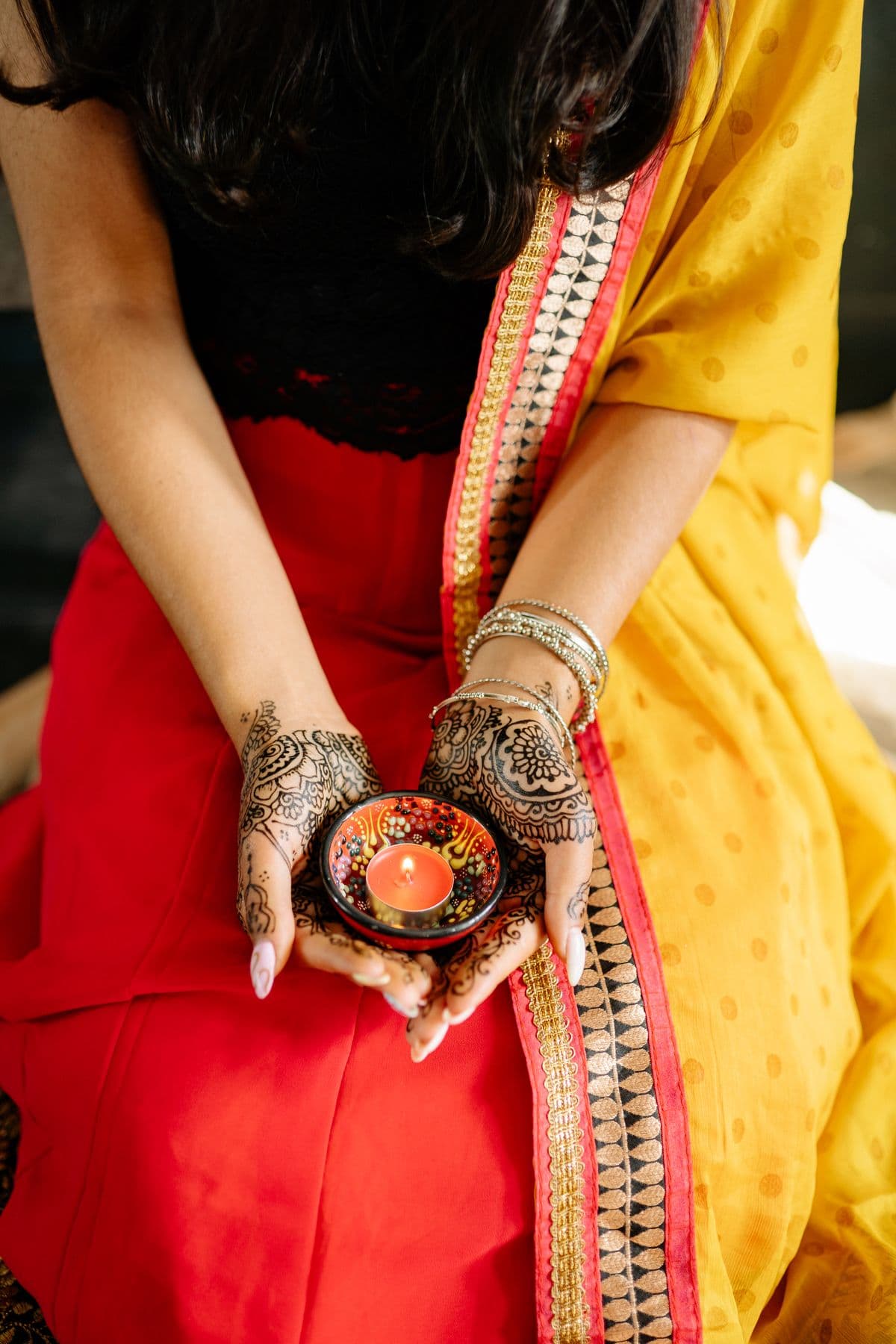 Hands decorated with mehendi, holding a small lamp